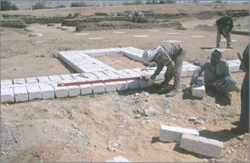 Masons at work laying the new stone blocks which mark the outline of the ancient stonework. The ancient layer of gypsum concrete which provides the evidence for the original presence of this stonework is buried beneath a thick layer of sand. The stone blocks are cut approximately to the ancient dimensions