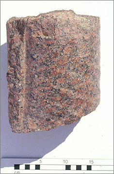 Fragment from a red granite statue from the North House Dump. It shows part of a leg clad in a pleated garment. 